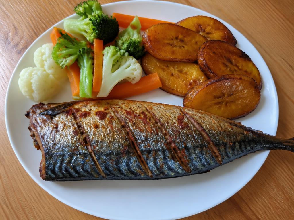 Plate of baked mackerel with roasted plantain slices and cooked vegetables