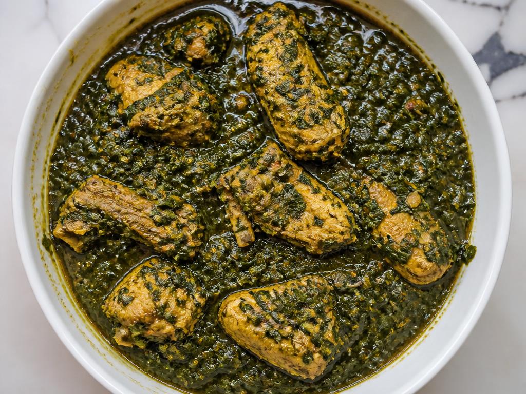 Bowl of Nigerian oha soup with green leaves and pieces of chicken
