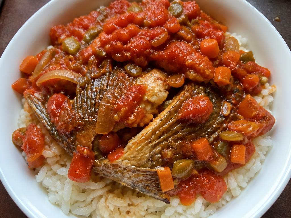 Bowl of rice topped with cooked tilapia in tomato sauce and vegetables