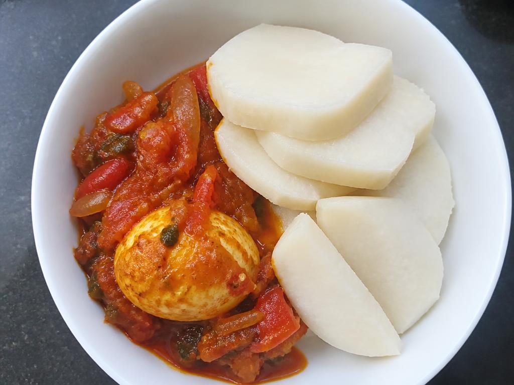 Bowl of boiled yam cubes with cooked egg sauce and mixed vegetables